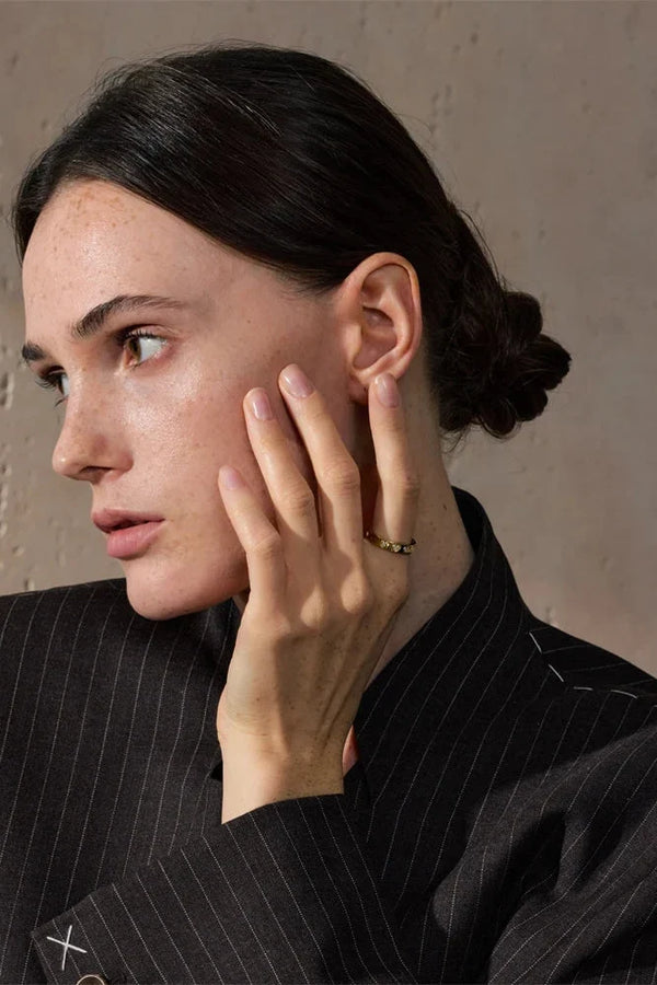 Woman in a black pinstripe suit with her hand near her face against a neutral background