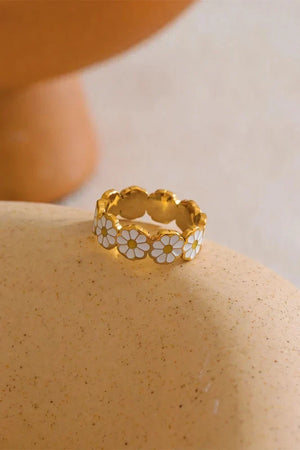 Gold ring with white floral designs on a beige surface