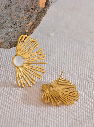 Gold sunburst earrings on a textured surface