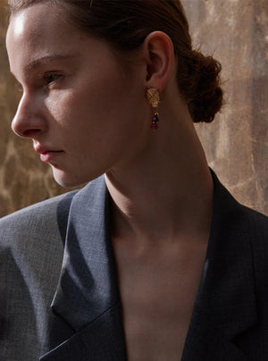 Woman wearing gold earrings with a stone wall background