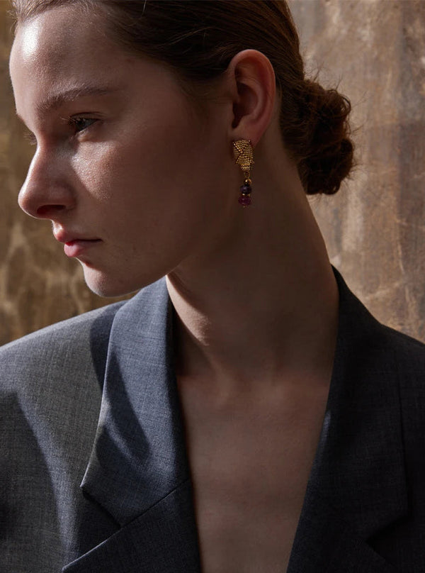 Woman wearing gold earrings with a stone wall background