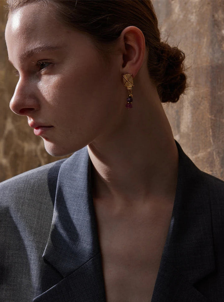 Woman wearing gold earrings with a stone wall background