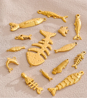 A set of gold-colored fish and fish skeleton charms arranged on a textured beige fabric background.