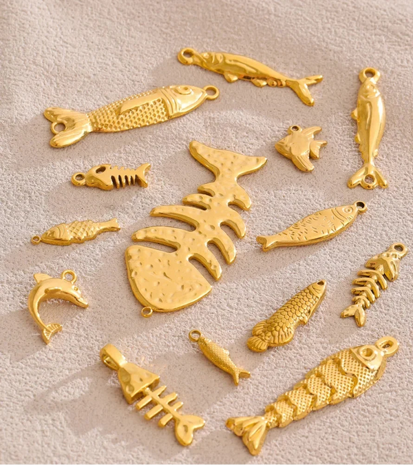 A set of gold-colored fish and fish skeleton charms arranged on a textured beige fabric background.