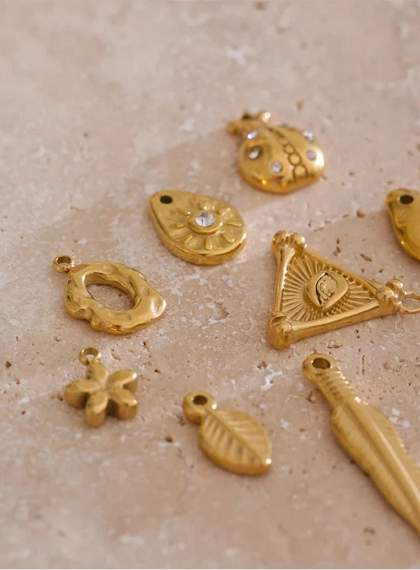 Collection of gold jewelry charms on a textured beige surface
