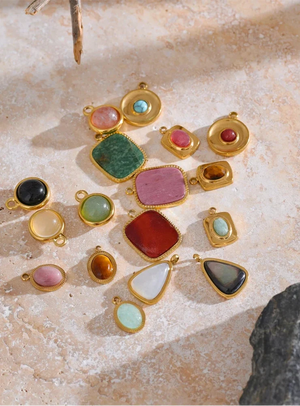 Collection of colorful gemstone pendants in gold settings on a textured stone surface