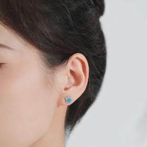 Close-up of an ear wearing a blue gemstone earring against a neutral background
