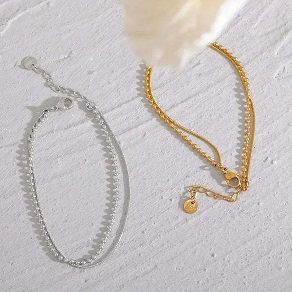 Silver and gold-plated chain bracelets with delicate clasps on a textured white surface