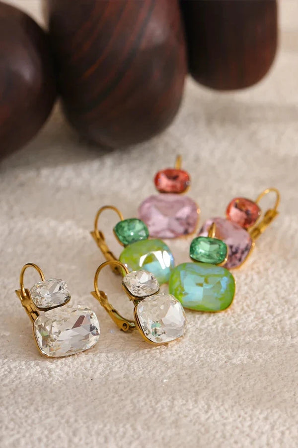 Pair of gold earrings with colorful gemstones on a textured surface.