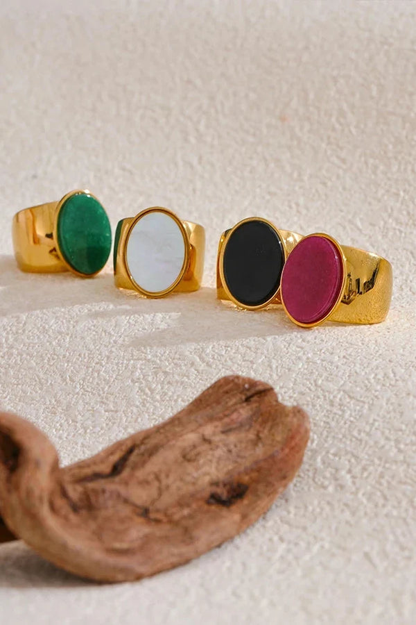 Four gold-rimmed rings with colored stones on a textured surface.