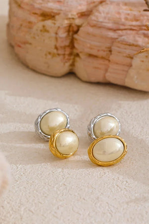 Pearl stud earrings with gold and silver accents on a textured surface.