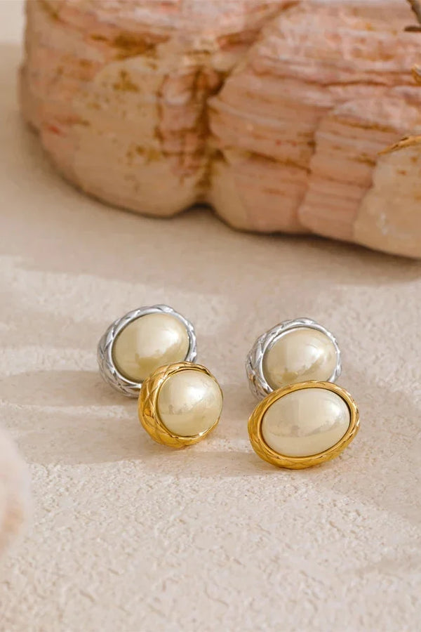 Pearl stud earrings with gold and silver accents on a textured surface.