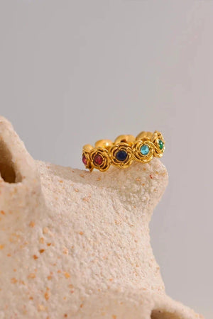 Gold ring with colored gemstones on a textured beige surface