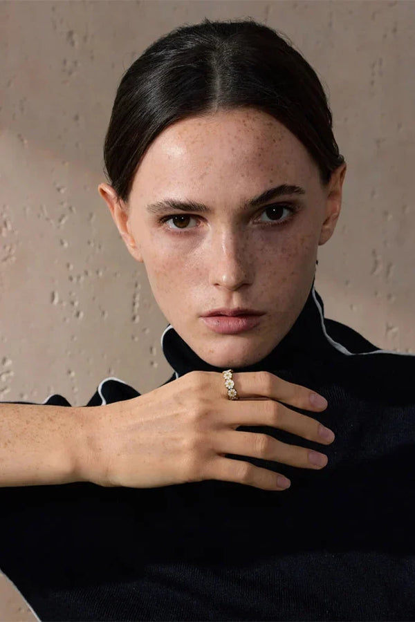 Woman wearing a black outfit with a close-up of her hand and ring against a neutral background
