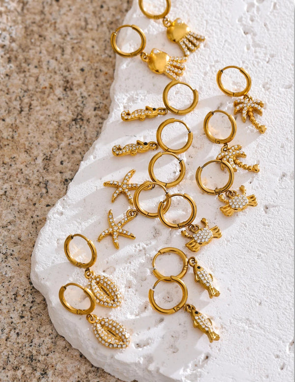 Gold jewelry charms on a textured white surface with 'SCENE DRAWING' text.