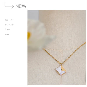 Gold necklace with a geometric pendant on a textured beige surface.