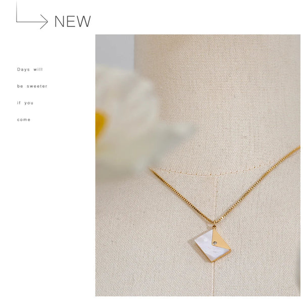 Gold necklace with a geometric pendant on a textured beige surface.