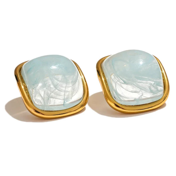 Pair of earrings with gold frames and light blue gemstones on a white background