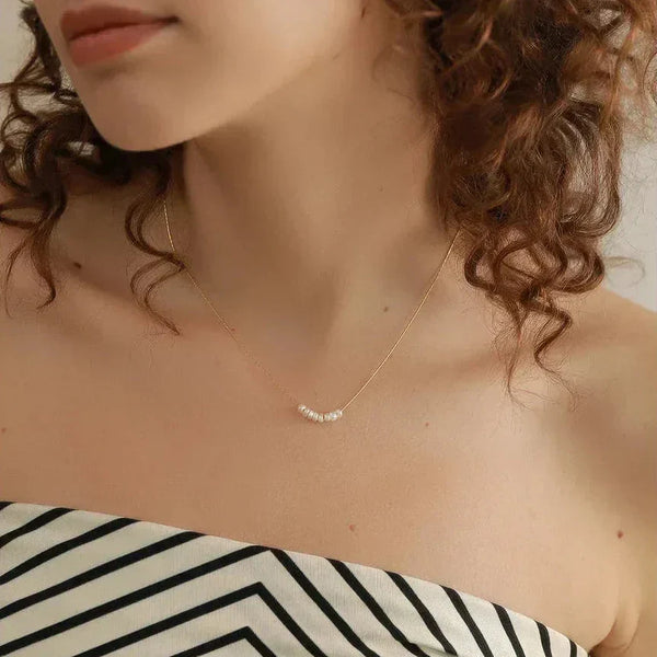 Woman wearing a delicate gold-plated necklace with small pearls, striped top, curly hair