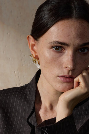 Woman wearing gold earrings with a neutral background