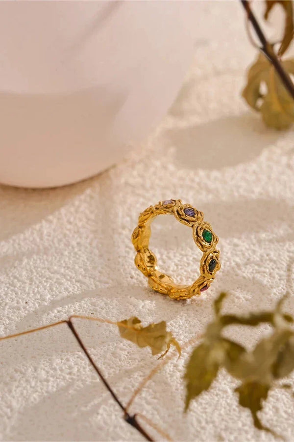 Gold ring with gemstones on a textured surface with a blurred background