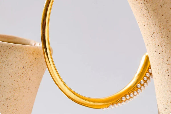 Close-up of a gold hoop earring with pearl accents on a light gray background
