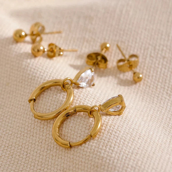 Gold hoop earrings with clear stones on a beige fabric background