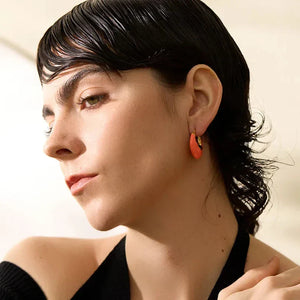 Woman wearing orange earrings with a neutral background