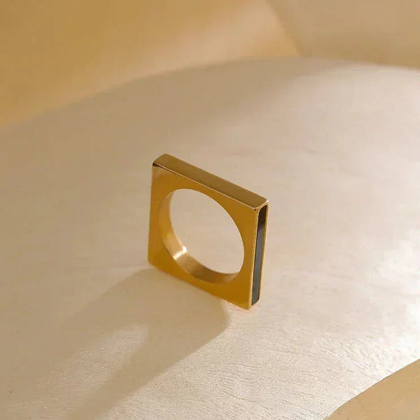 Square gold-plated ring with minimalist design on a neutral background