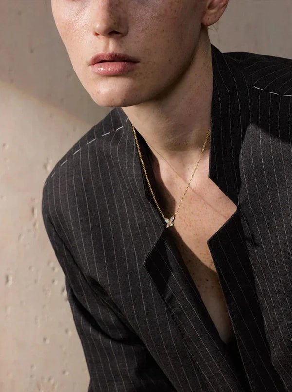 Person wearing a black pinstripe suit with a necklace against a neutral background