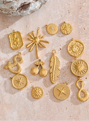 Collection of gold jewelry charms on a textured beige surface