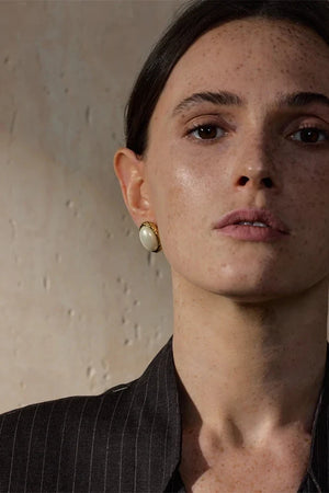 Close-up of a woman wearing a gold earring against a neutral background
