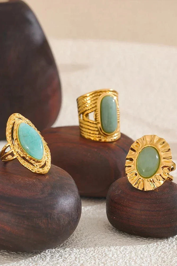 Three gold rings with green stones on wooden stands.