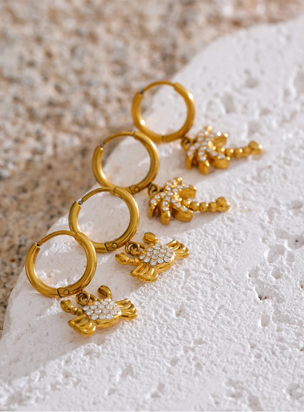 Gold hoop earrings with floral designs on a textured white surface