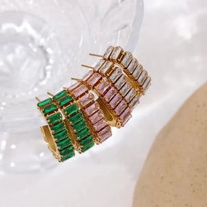 Gold hoop earrings with green and pink gemstones on a textured white surface