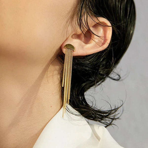 Gold fringe earring worn by a person with a neutral background
