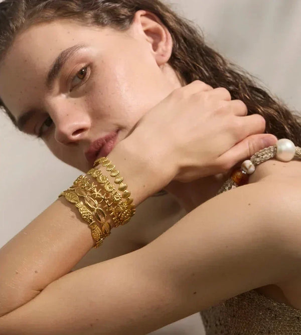 Woman wearing gold bracelets with a neutral background