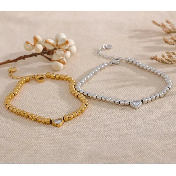 Gold and silver beaded bracelets with heart charms on a beige fabric background