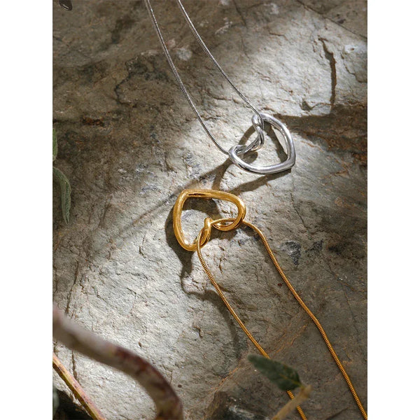Gold and silver heart-shaped pendant necklaces on textured stone surface