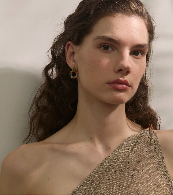 Woman wearing a one-shoulder beaded top against a neutral background