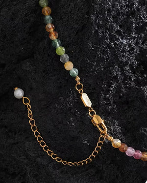 A beaded necklace with multicolored round gemstone beads and gold-tone chain hardware, laid on a dark textured surface.