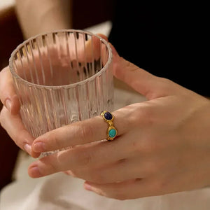 Woman wearing a gold-plated silver ring with blue and turquoise stones, holding a glass