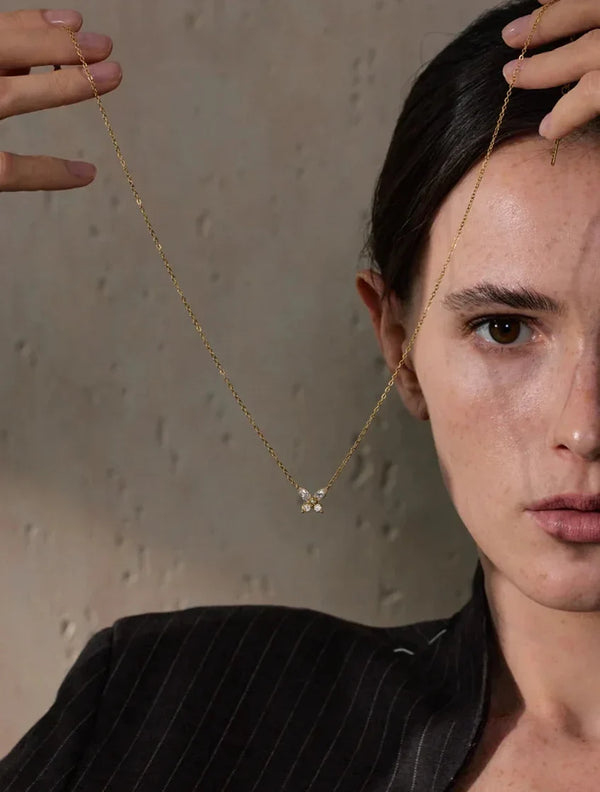 Woman wearing a delicate gold necklace with a small pendant against a neutral background