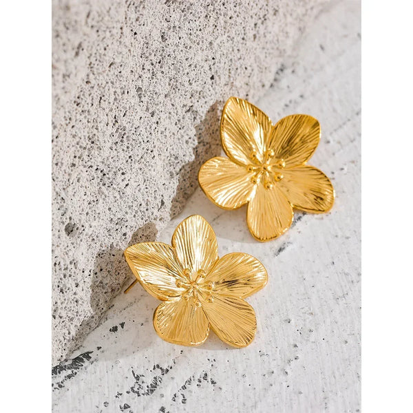 Gold-plated flower-shaped earrings on textured stone surface, elegant jewelry accessory