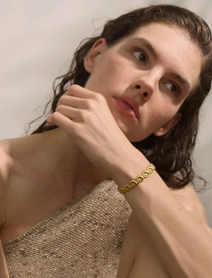 Woman with wet hair wearing a gold bracelet on a plain background