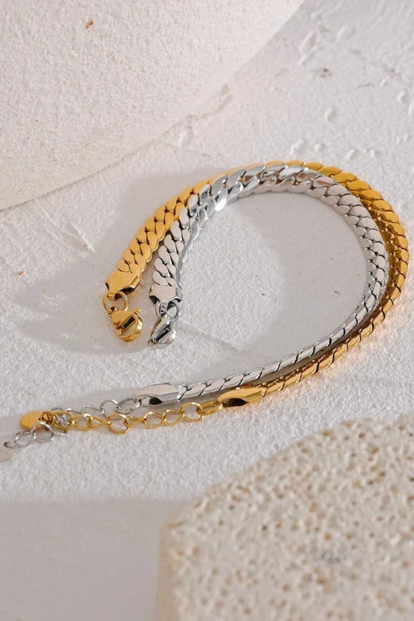Two gold and silver chain bracelets on a textured white surface