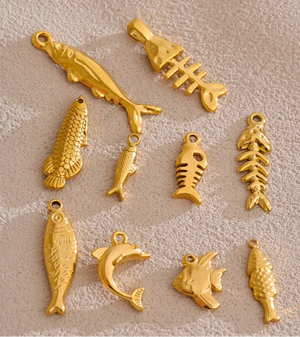Nine gold-colored fishing-themed charms, including fish, fish skeletons, and a jumping fish, arranged on a textured beige background.