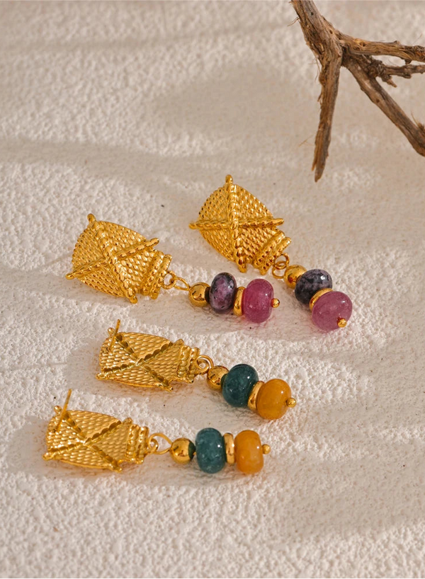 Gold earrings with colorful beads on a textured beige surface