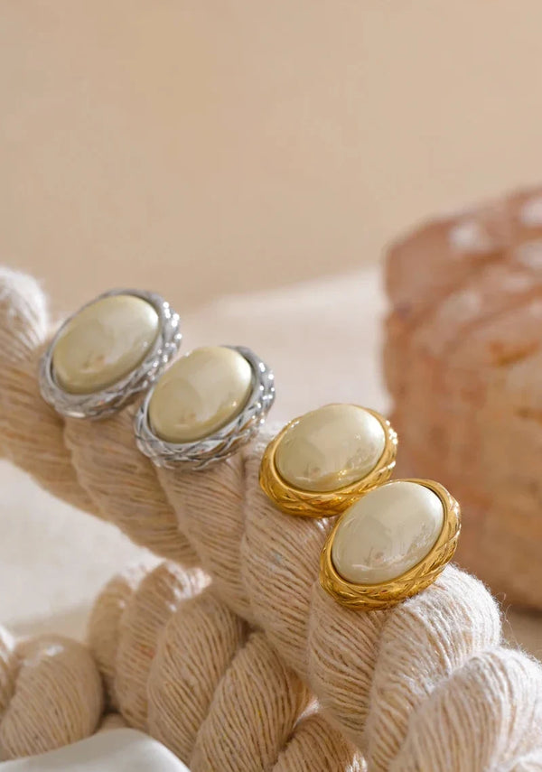 Pair of earrings with beige stones and gold accents on a textured beige background