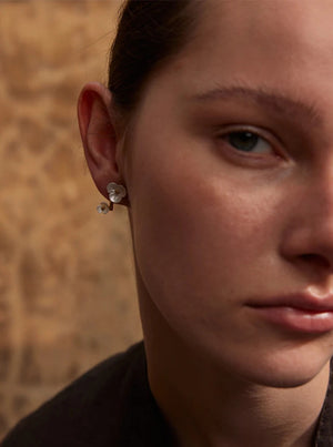 Close-up of a person wearing pearl earrings with a blurred background